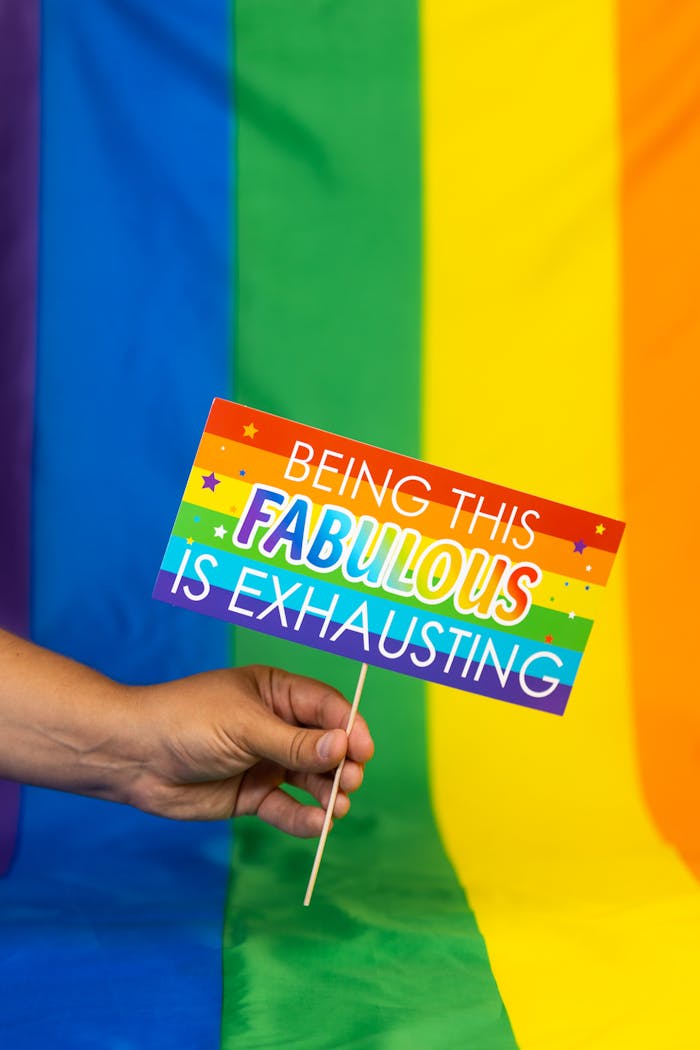 Close-up of a hand holding a Pride-themed sign with rainbow colors.